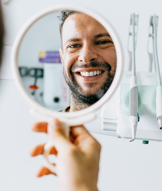 A person holding up a magnifying mirror towards their face, smiling at the camera.